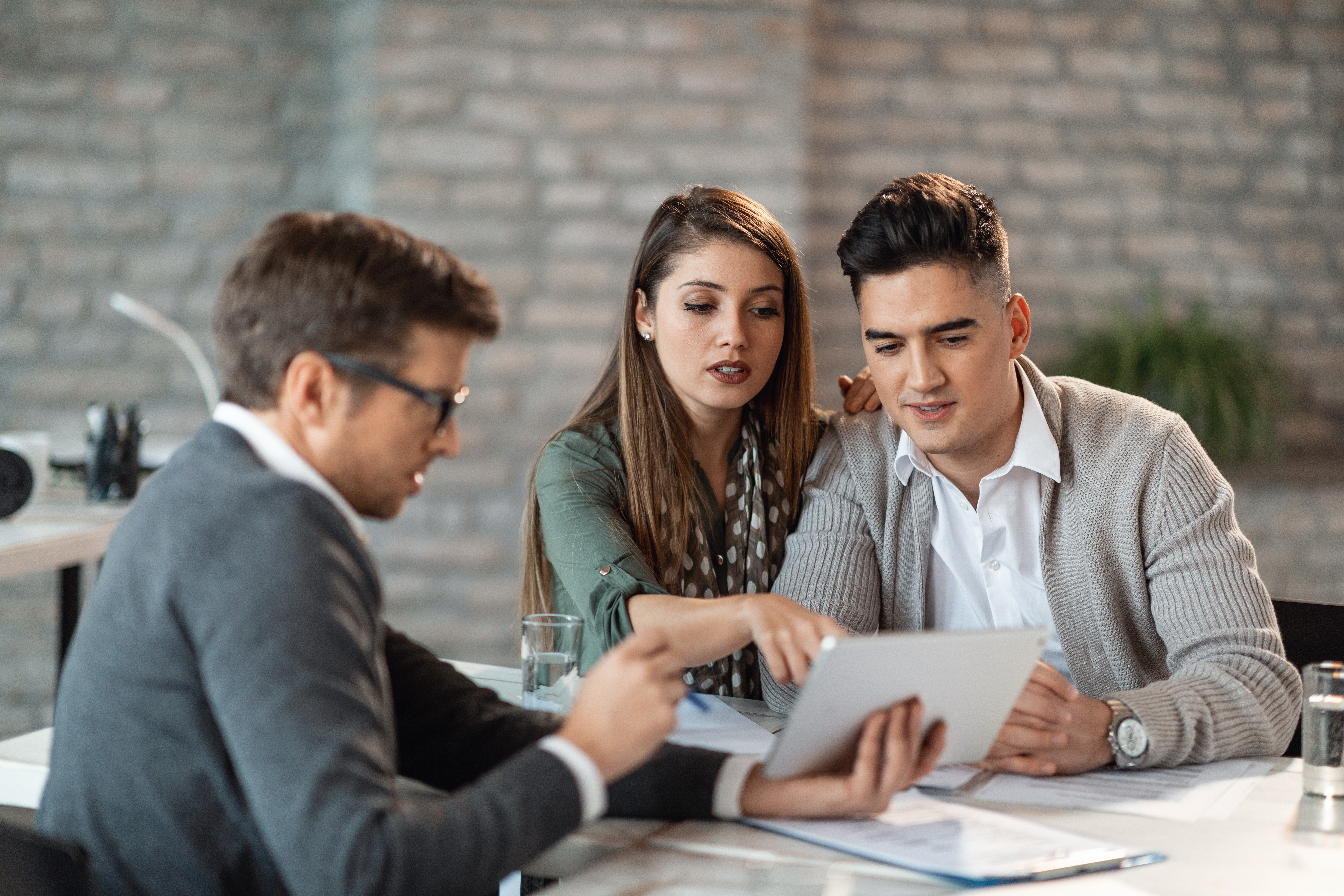 young couple using touchpad with insurance agent while making loan repayment plan meeting
